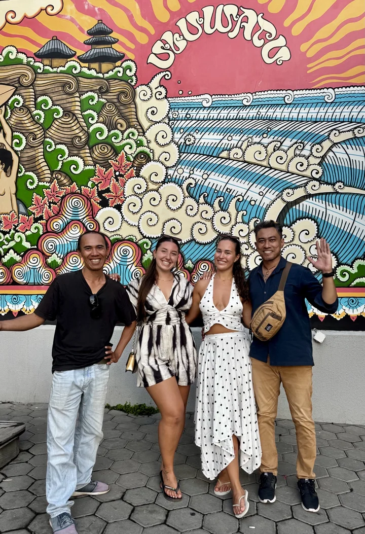 Nyoman and Putra with guests in front of a colourful Uluwatu mural